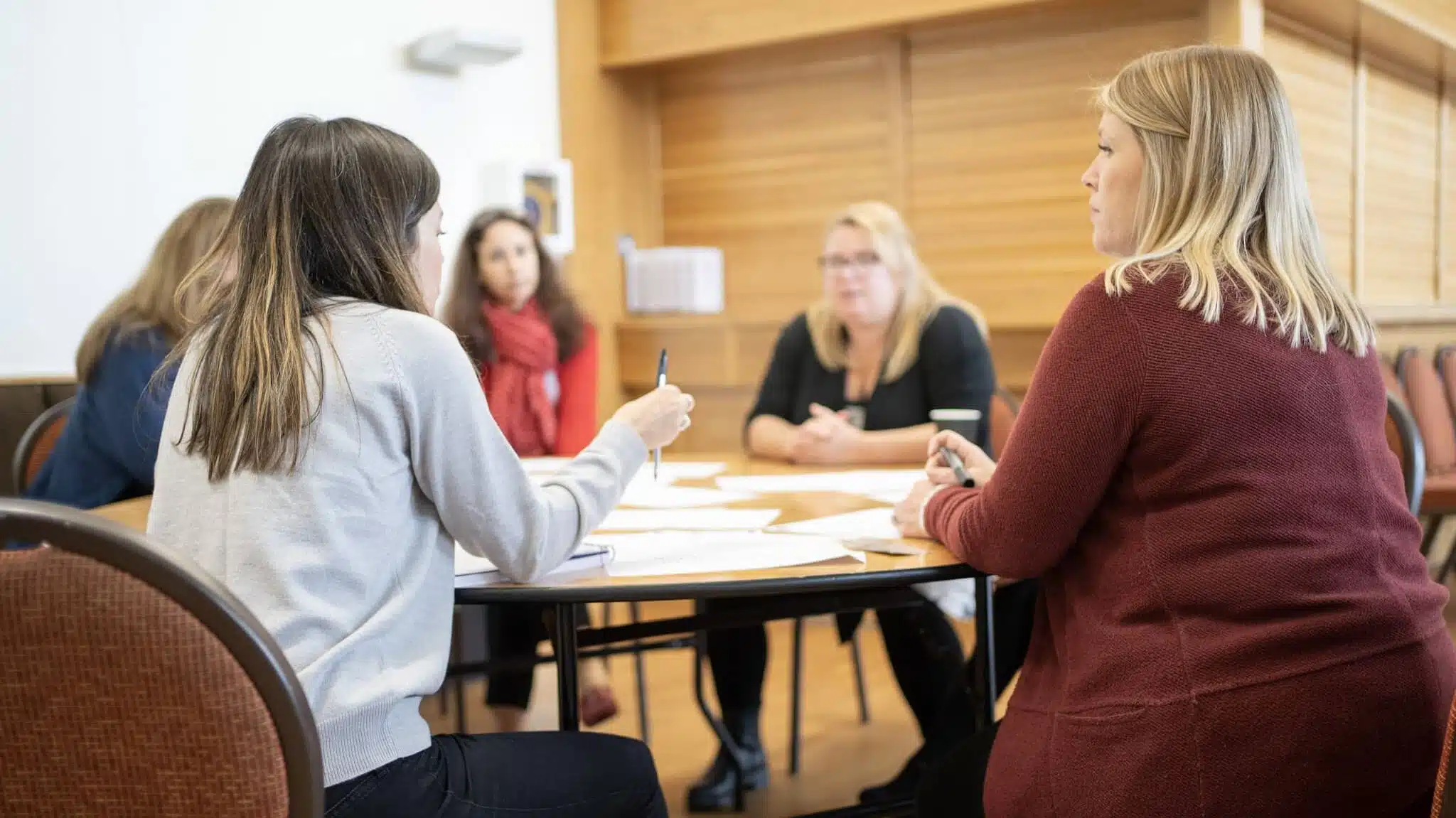 A photo of five people sitting around a circular table, discussing market research methods