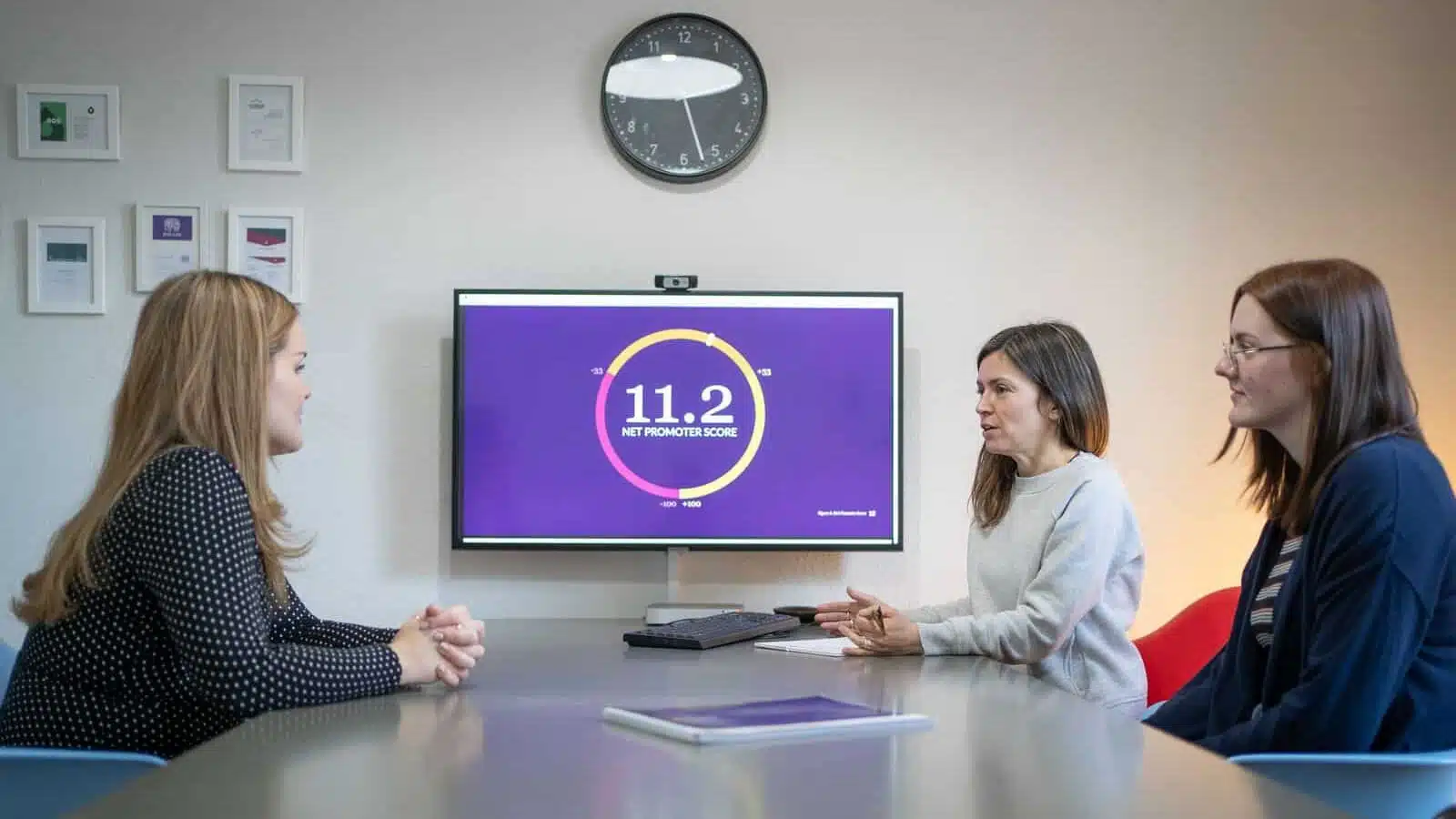 Three people sit at a table next to a screen displaying data visualisation of a Net Promoter Score